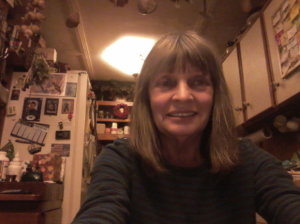 A woman sitting in her kitchen, smiling at the camera. She's got short hair with bangs and is wearing a striped sweater.