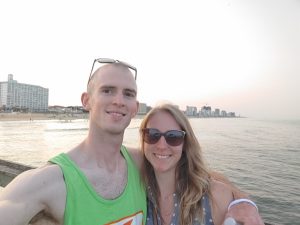 A selfie of a couple standing near the water, smiling.