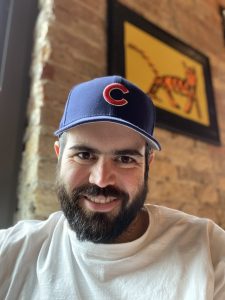 A bearded man in a Chicago Cubs hat smiles at the camera