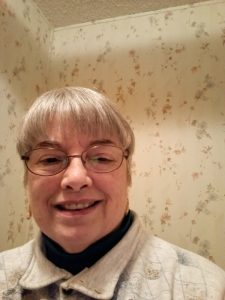 Judith smiles at the camera. She is wearing glasses and a turtleneck.