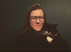 Tori smiling at the camera holding her cat named Rory, who is definitely not smiling.