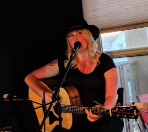 Blythe playing the guitar, dressed in all black.